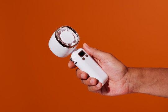 a man grips a white handheld fan with chrome rim on an orange setting