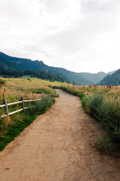 Panorama of a dirt road crossing an open field with wooded mountains