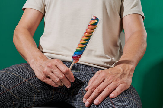 man holds a wrapped spiral lollipop against a green background