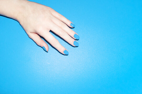 Bright blue beauty painted manicure nails on blue surface