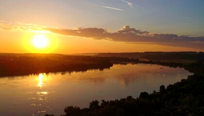 A golden sunrise over a wide river, with sun reflecting on water and trees lining banks