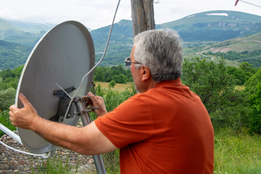 Man Adjusting Satellite Dish in Scenic Mountains