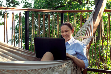 Middle aged woman with laptop in a hammock on the hotel terrace.