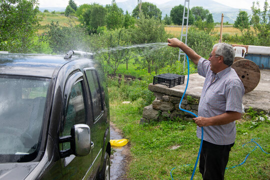Man Washing Vehicle Using a Hose in a Countryside Backyard Setting