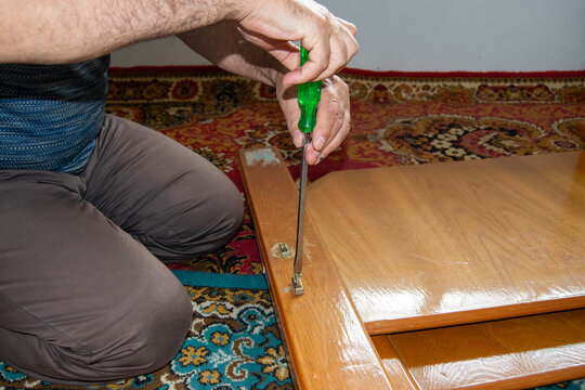 A man repairing wooden furniture using a screwdriver on a colorful rug