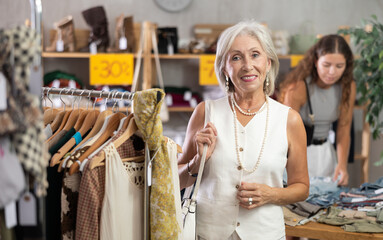 Happy mature woman standing posing cheerfully in clothing store during shopping