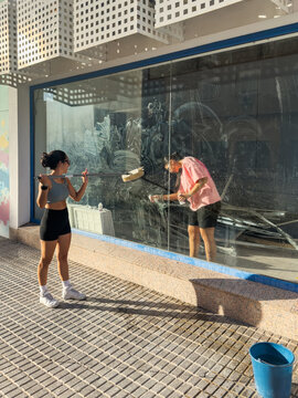 Two Young Women Cleaning Large Storefront Window Inside and Outside