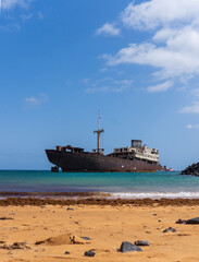 Rusting shipwreck anchored in turquoise waters near the rocky coast of Lanzarote, Canary Islands.