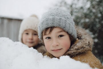 Two children are playing in the snow, one wearing a hat