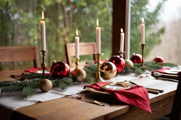 Christmas table setting decorated with candles, ornaments, garland, and red napkins