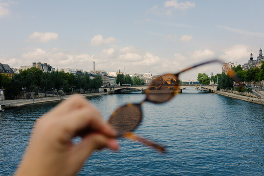 Tourist holds sunglasses with Seine River visible in the background