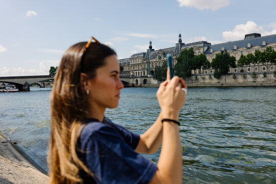 Female tourist taking photos of the Seine River and the Louvre Museum
