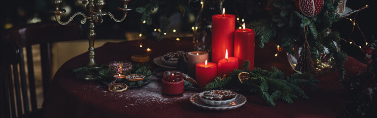 Christmas and New Year beautiful elegant family dinner table setting decorated with red candles, fir tree branches, homemade gingerbread cookies. Banner