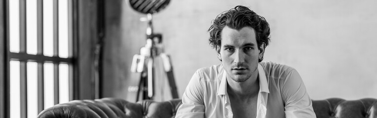 Banner. Black and white portrait of strong healthy elegant handsome sexy athletic man in leather coat in a stylish loft interior, wearing suit, watches. Male model posing and smiling