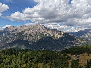 High mountain landscape in the French Alps, forest and rocky peaks near Briançon – Aerial view with chalets
