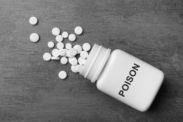 Bottle with Poison label and pills on grey textured background, top view