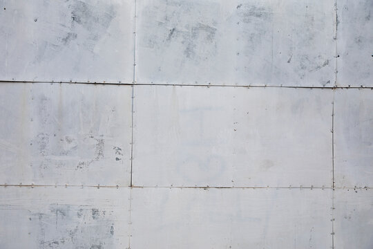 Weathered gray metal panel texture with visible seams and rivets.