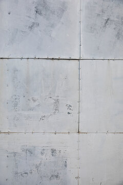 Weathered gray metal panel texture with visible seams and rivets.