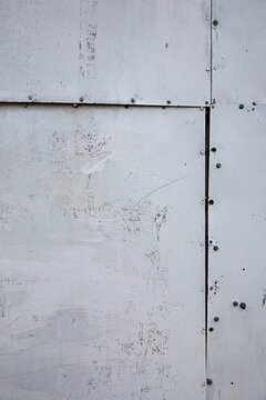 Weathered gray metal panel texture with visible seams and rivets.