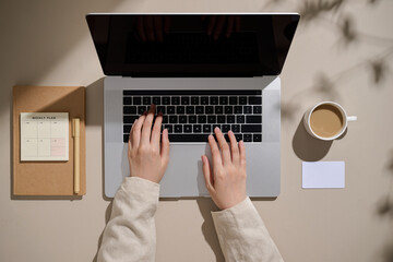 A person is working on a laptop, with coffee and planner
