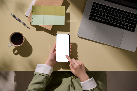 A person interacts with their smartphone at a desk next to coffee cup