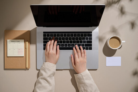 A person is working on a laptop, with coffee and planner