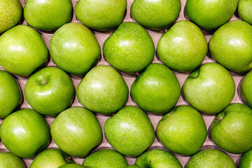 Fresh green apples arranged in a neat pattern on a wooden surface, showcasing their vibrant color...