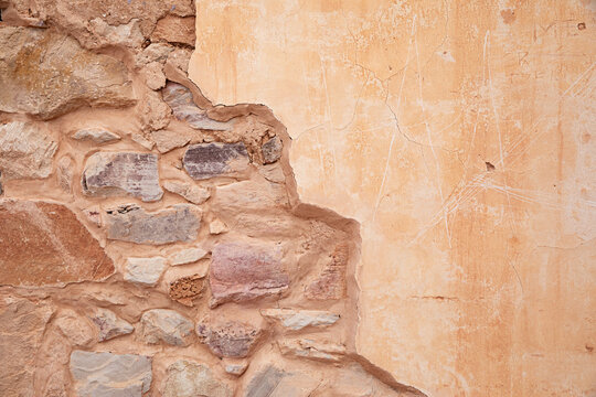 A weathered stone wall with stucco reveals an aged, textured surface.