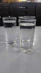 Curated image of three glasses of water stand on a white table in a restaurant setting.