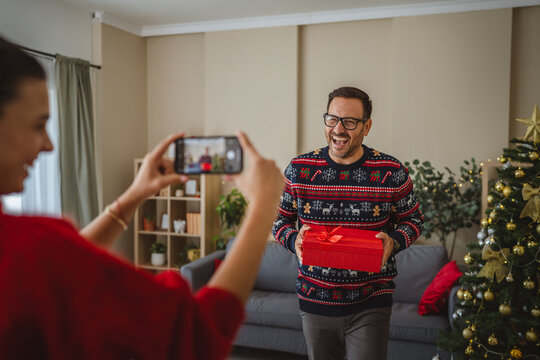 Woman taking photo of man holding christmas gift