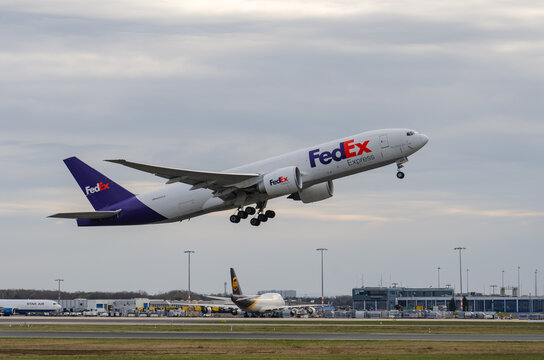 A Boeing B777 from FedEx during takeoff and a Boeing B747 from UPS at the Apron in the background.