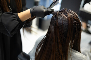 Naklejka premium A woman with long dark hair receiving a hair treatment at a salon, showcasing the expertise of her stylist.