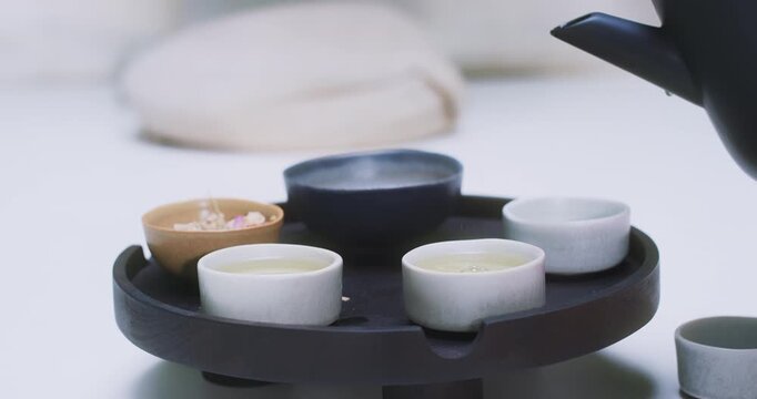 Teapot pouring tea into cup on serving tray, close-up