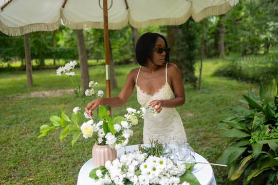 Woman Arranging Flowers Under an Umbrella in a Lush Garden Setting