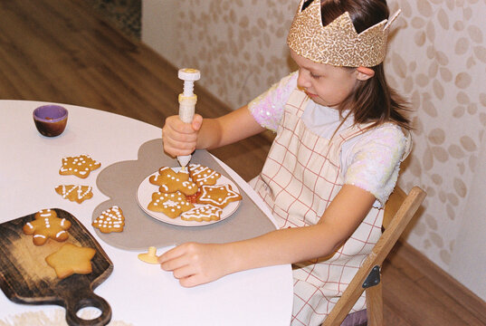Girl painting gingerbread cookies with white icing by pastry bag.