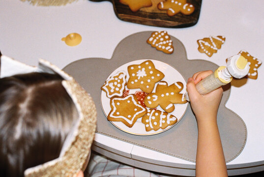Girl painting gingerbread cookies with white icing by pastry bag.