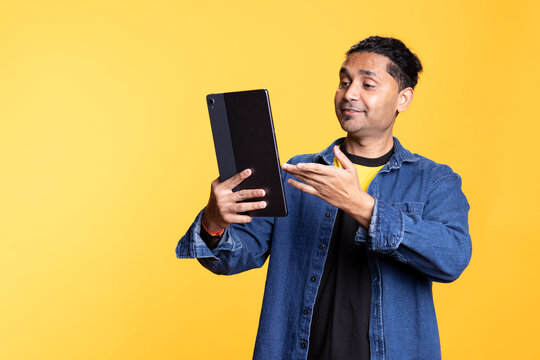Confident friendly guy meeting with his friends on online web conference, uses his tablet to chat remotely with people. Young indian person having a joyous entertaining conversation.