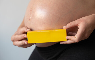 Pregnant woman holding yellow medicine box in front of belly