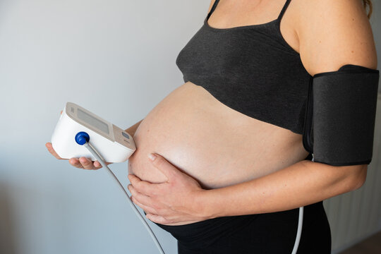 Pregnant woman monitoring blood pressure using a digital sphygmomanometer at home