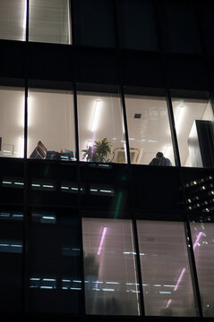 Office worker seen through window at night in city building