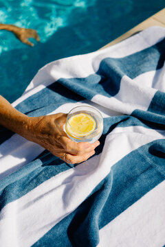 Unknown hand holding a glass of natural lemonade t the edge of a pool