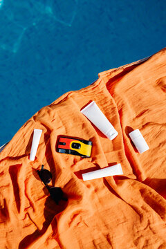 Close-up overhead of sunscreen, camera and sunglasses on towel by pool