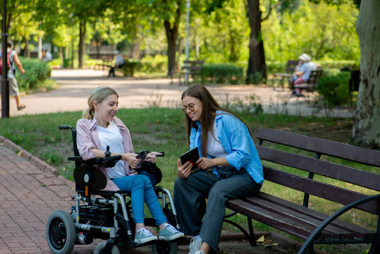 Young woman in a wheelchair and her colleague talk in a city park