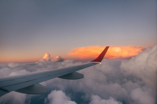 Airplane wing soaring through clouds during sunset
