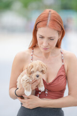 A woman holding a small dog. The dog is brown and white. The woman is wearing a red top