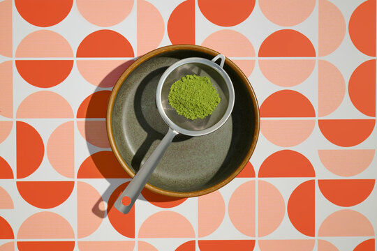 Sifting matcha powder into a bowl on a patterned background