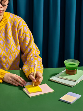 A person with glasses writes on a sticky note with a pen