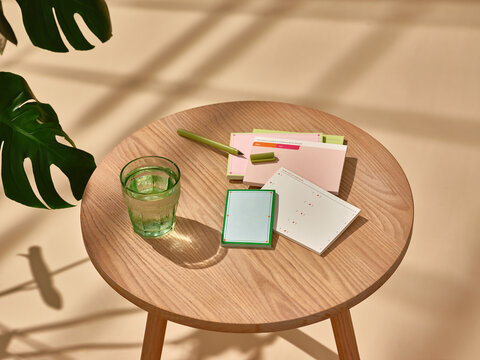 Elegant glass of water and notepads on table under sunlight