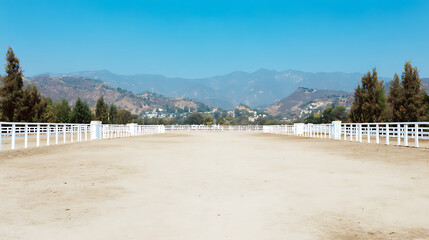 Obraz premium Empty dirt track with white railings and mountainous background under clear blue sky