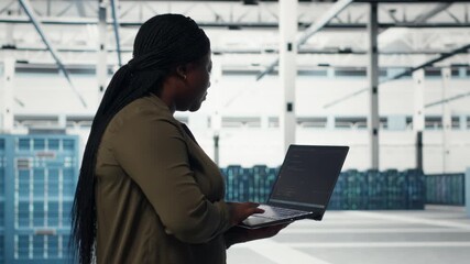 Technician with laptop walks through data center server rows, implementing advanced power management solutions. Worker using notebook to oversee server hub, reducing energy consumption, camera B - Powered by Adobe